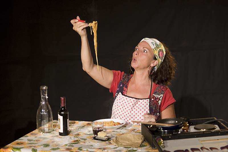 La protagonista, seduta al tavolo, ha davanti a sé un piatto di spaghetti al sugo e si accinge a mangiarli