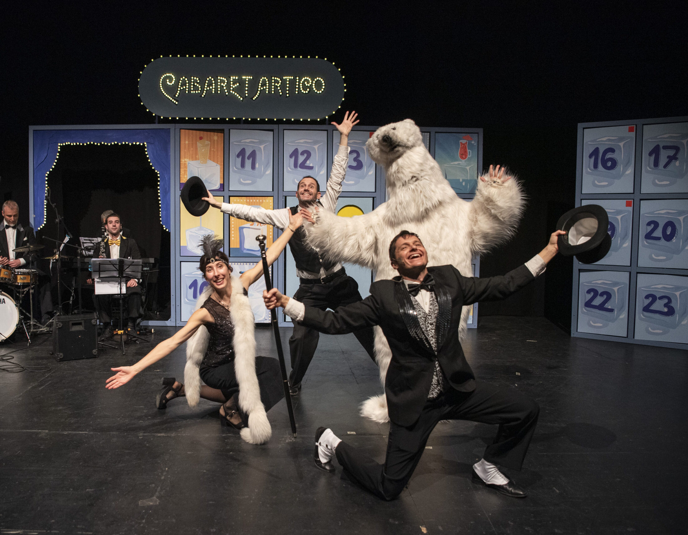 Foto degli attori dell'attrice sul palco, insieme all'orso polare e ai musicisti dietro di loro, durante il finale dello spettacolo, alcuni in ginocchio altri in piedi, con le braccia allargate e grandi sorrisi mentre salutano il pubblico