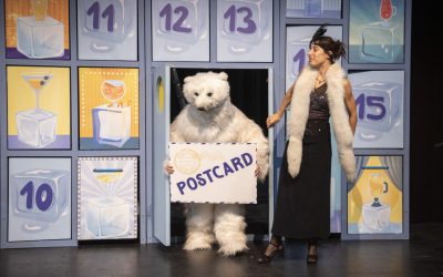 Sul palco un'attrice apre una porta da cui esce un attore vestito da orso bianco con un'enorme cartolina in mano
